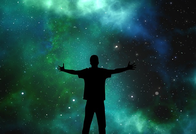 Foto noturna de um homem de braços abertos voltado para o céu estrelado